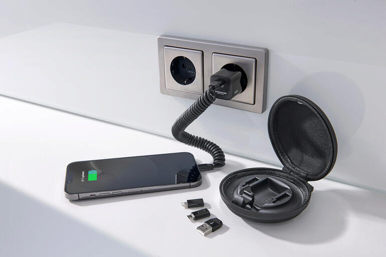 Smartphone, chargeur et accessoires sur une table, entourés d'une prise murale.