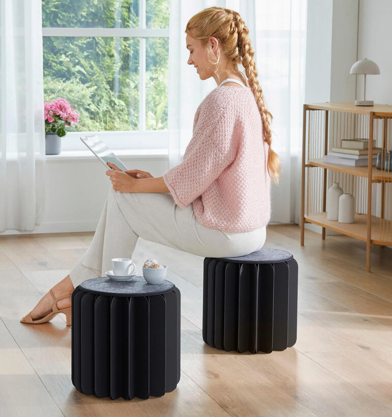 Femme sur un pouf Bookniture avec une tablette dans une pièce élégante.