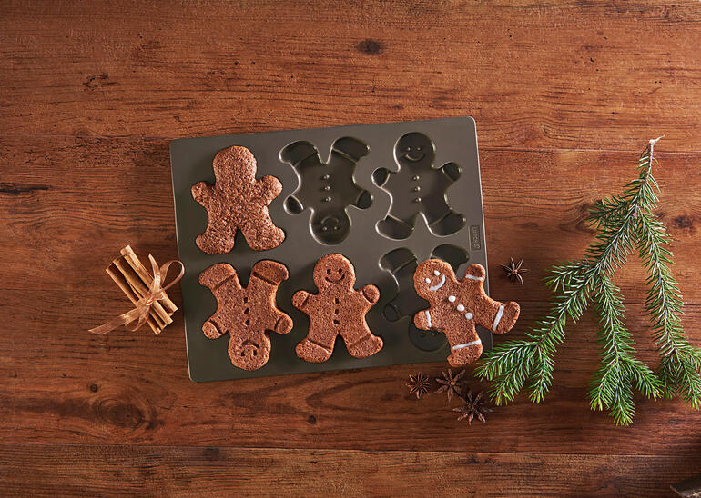Moule à biscuits en pain d'épices avec des bonhommes en pain d'épices cuits sur une table.