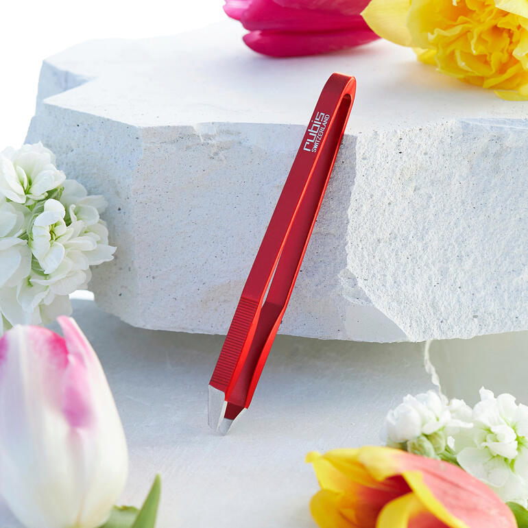 Pince ultralégère rouge posée sur une surface en pierre blanche, entourée de fleurs.