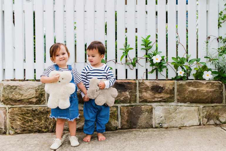 Deux enfants se tiennent contre un mur, souriant tout en étreignant des ours en peluche en peau de mouton.