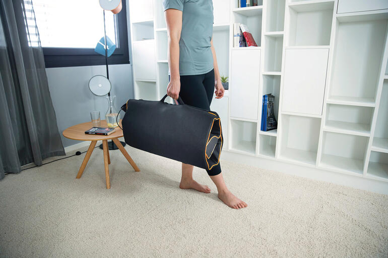 Rangé au format sac en clin dʼœil après utilisation. Idéal également en voyage. Homme portant un tapis d'étirement et de massage dans un sac