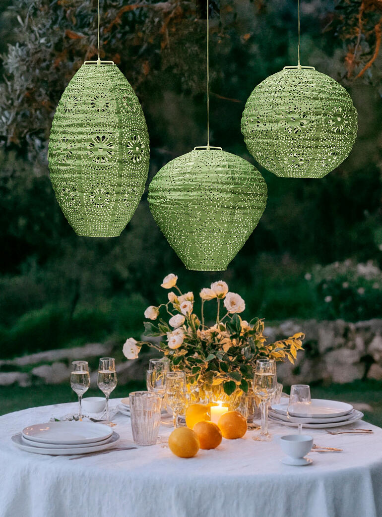 Même lorsqu’elles sont éteintes, les lanternes seront un tape-à-l’oeil fascinant. Trois lanternes étanches en sauge avec panneaux solaires et LED au-dessus d'une table dressée.