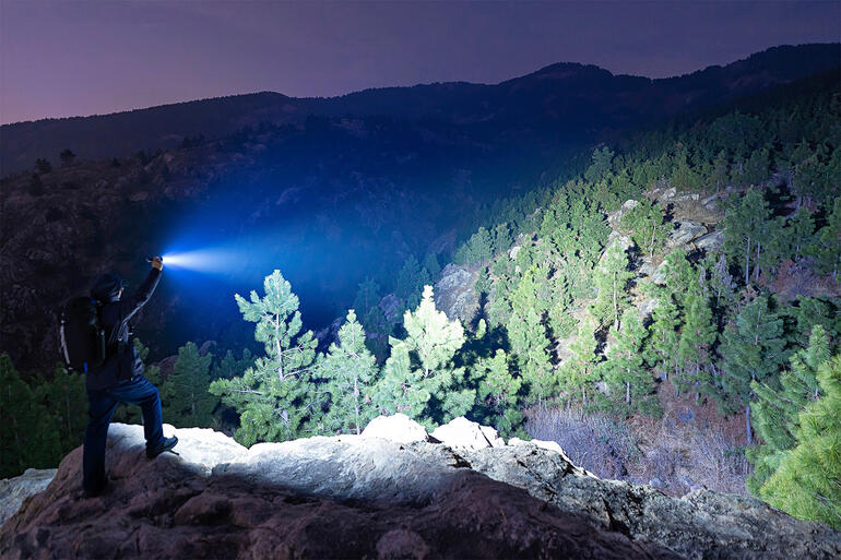 Les 6 LEDs à haut rendement offrent une lumière projetée dʼincroyables 5 000 lumens et la font rayonner jusquʼà 245 m de distance. Homme tenant une lampe de poche dans les montagnes la nuit.