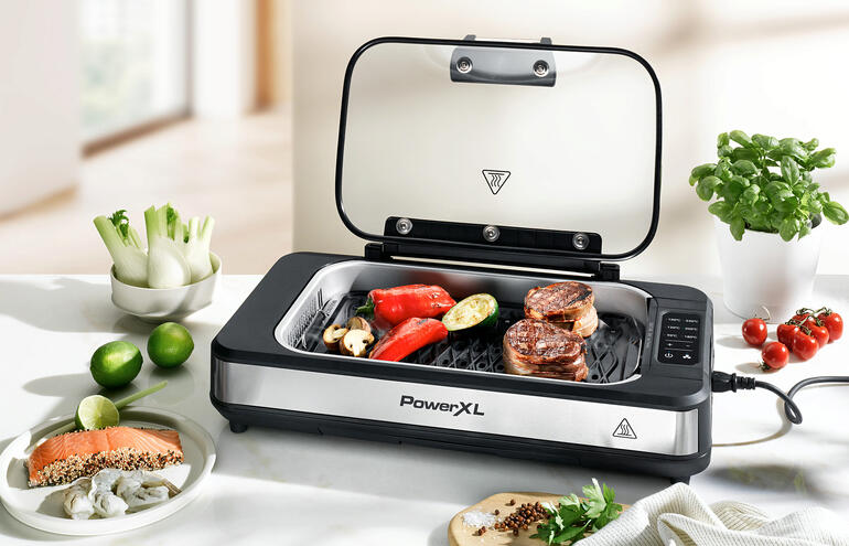 Gril de table avec couvercle ouvert et légumes et viandes dessus.