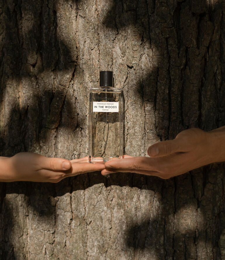 Bouteille In the Woods Eau de Parfum dans les mains, devant un tronc d'arbre.