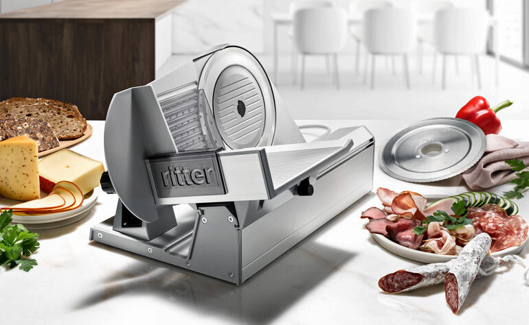 Trancheuse Tondo 13 sur un plan de travail de cuisine avec de la viande, du fromage et des légumes.