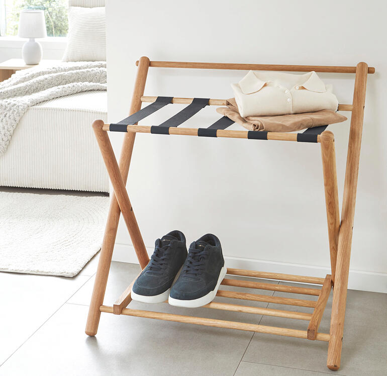 Idéal également comme espace de rangement pour les vêtements qui ne doivent pas encore être lavés, mais ne doivent pas non plus être rangés au placard. Support de bagages en chêne avec des vêtements pliés et des baskets dessus.