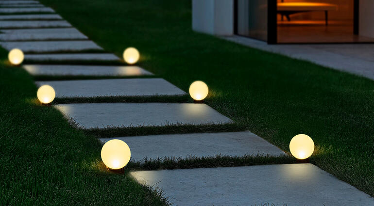 Grâce aux piquets de terre inclus, vous pouvez placer les lampes solaires le long d’un chemin, dans des parterres, des jardinières de balcon... Lampes solaires globe sur un chemin, éclairées, menant à un bâtiment moderne.