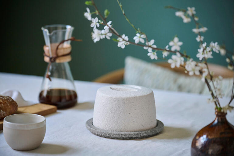 Beurrier en céramique sur une table avec des fleurs et une cafetière.