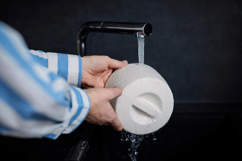 Personne nettoyant un beurrier en céramique sous l'eau courante.