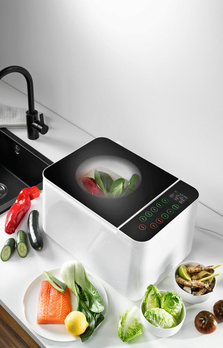 Appareil de lavage de nourriture sur le comptoir, entouré de légumes frais.