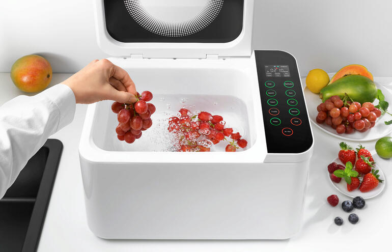 Mettez-y par exemple simplement des fruits et sélectionnez le programme approprié – le processus de nettoyage commencera. Main prenant des raisins dans le nettoyant alimentaire pendant que l'eau bouillonne.