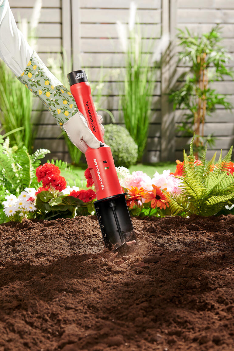 Tarière sur batterie Perceuse à batterie dans la terre avec des fleurs en arrière-plan