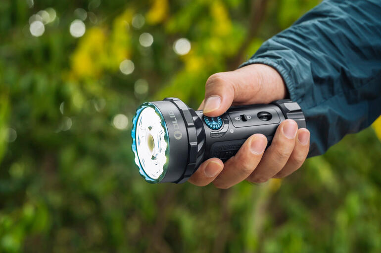 Commutable intuitivement par simple pression du pouce. Homme tenant une lampe de poche à l'extérieur avec un fond vert.