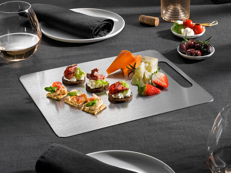 Idéale également pour dresser et servir. Planche à découper en titane avec différents amuse-gueules sur une table