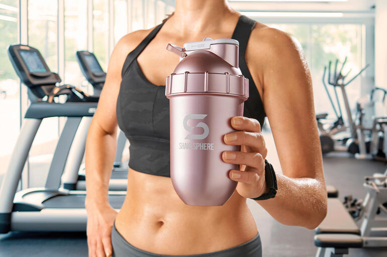 Femme tenant un shaker rose dans une salle de sport.