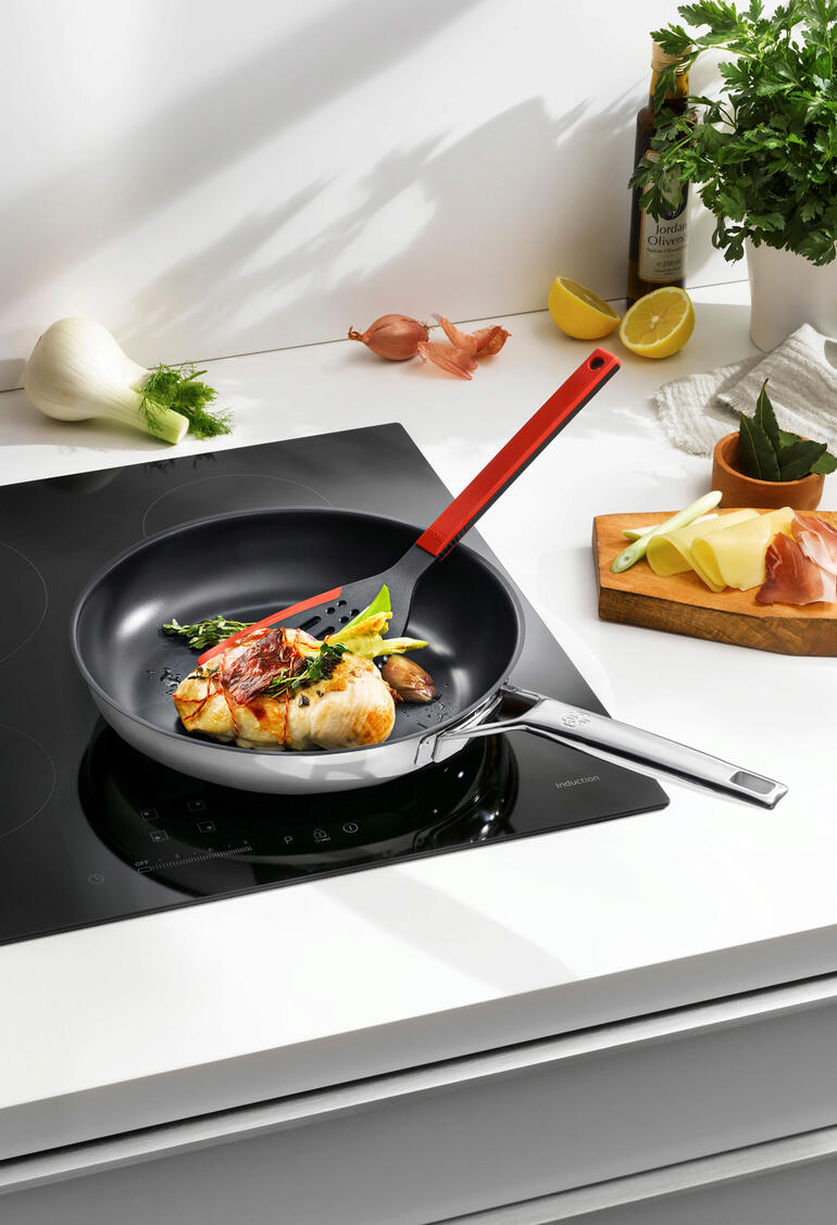 Poêle en acier inoxydable avec effet antiadhésif, remplie de légumes et de poisson sur une cuisinière.