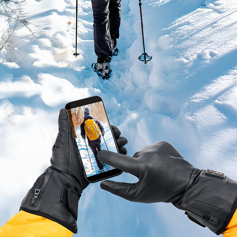 Main avec smartphone montrant l'utilisateur dans un cadre enneigé.