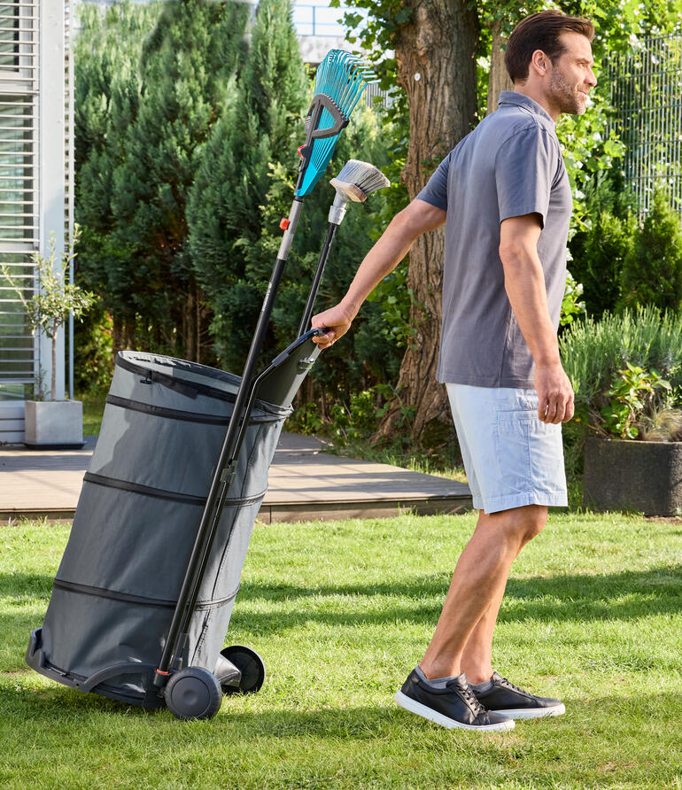 Homme tirant un chariot de jardin pliable avec des feuilles dans le jardin.