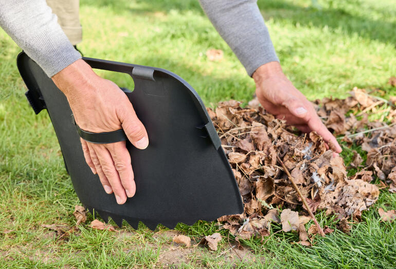 Amovible en une seule étape : la pelle à main intégrée. Gros plan de mains soulevant des feuilles avec une pelle.