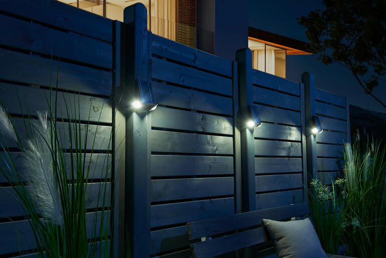 Le lot de trois convient également pour éclairer des zones plus grandes. Projecteur solaire intelligent éclairant une clôture en bois la nuit.