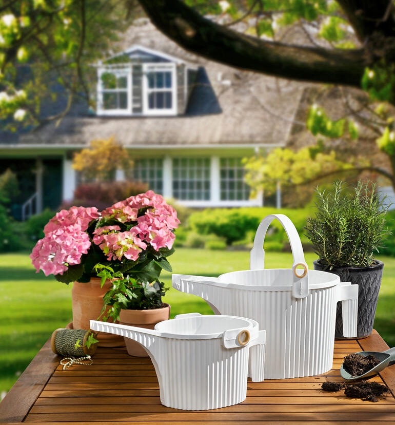 Deux arrosoirs en blanc et des fleurs sur une table au jardin