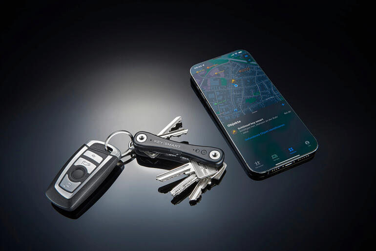 Une fois votre KeySmart® iPro localisé, vous verrez sa position dans l’application « Localiser mon » sur votre iPhone. Organisateur de clés intelligent à côté d'un porte-clés et d'un smartphone sur une table.