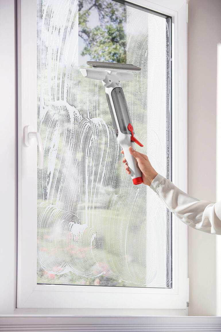 Personne nettoie une fenêtre avec un lave-glace télescopique 3-en-1, solution savonnée sur le verre.