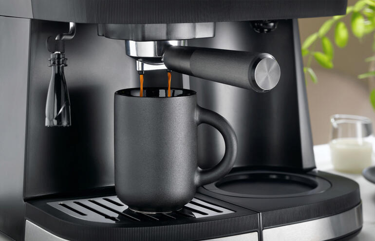 Tasse noire placée sous un robinet d'espresso.