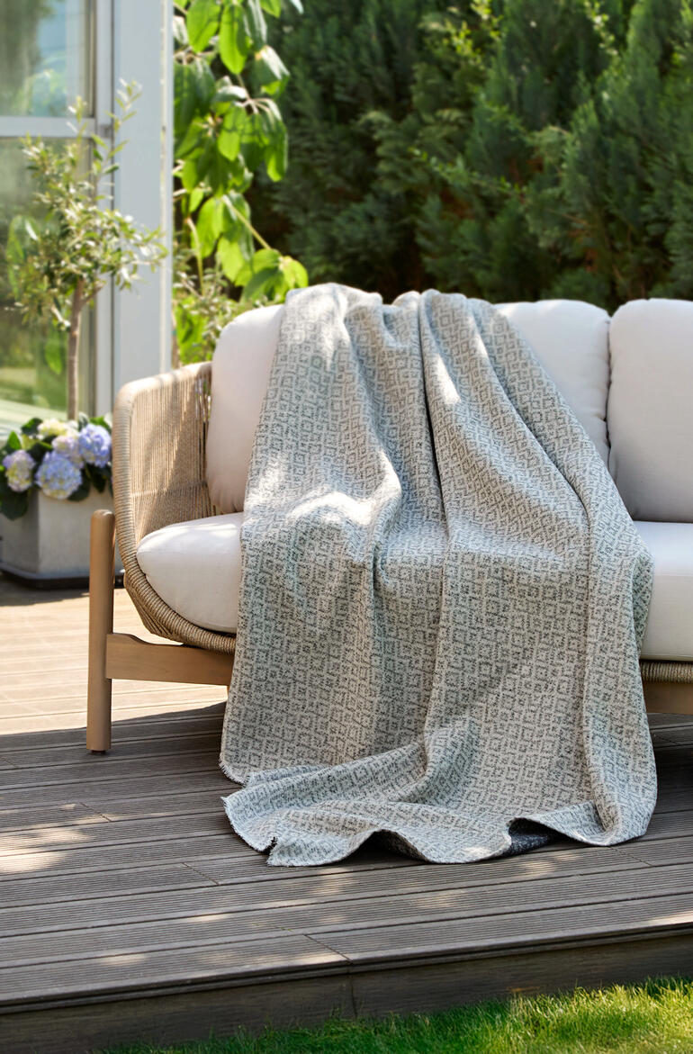 Couverture réversible en jacquard posée sur un banc de jardin.