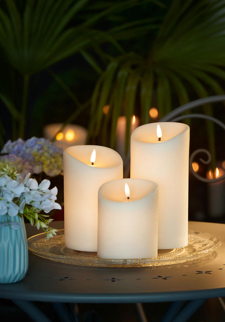 Trois bougies LED en cire d'extérieur sur une table en plein air.