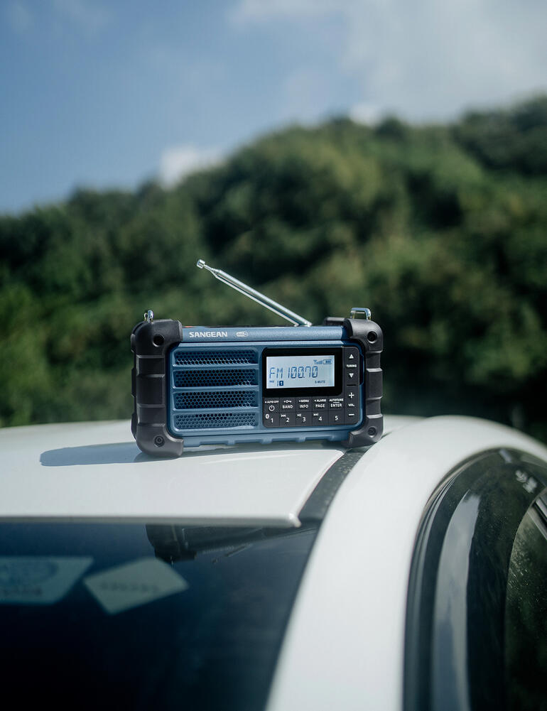 Radio noir sur une voiture avec antenne, arrière-plan montrant un paysage vert.