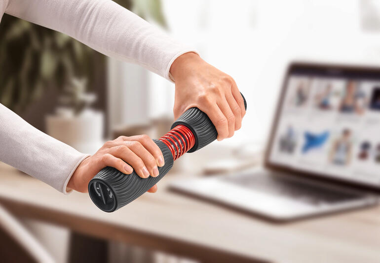 Personne s'entraîne avec un entraîneur de poignet et d'avant-bras sur une table avec un ordinateur portable.