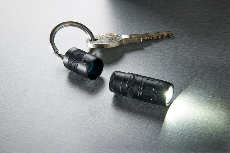 Mini-lampe de poche magnétique et clé sur une surface brillante, lampe s'allumant.
