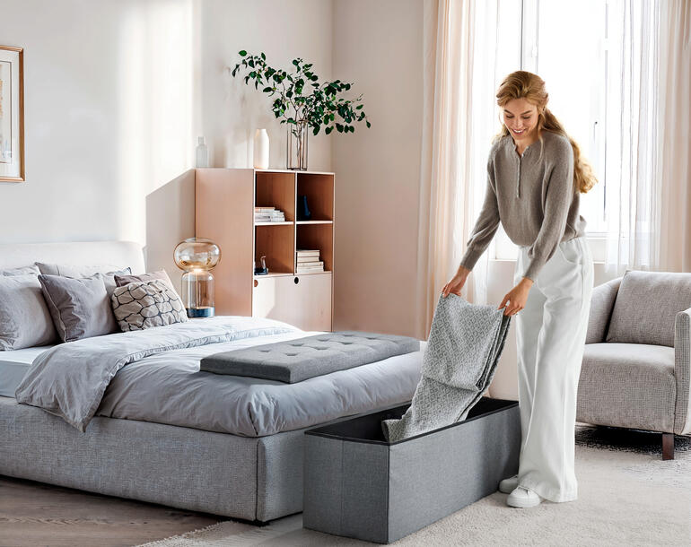 Coffre à siéger pliable en gris foncé, utilisé dans la chambre.