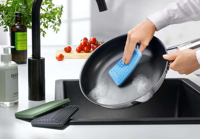 Personne nettoie une poêle avec une éponge en silicone bleue.
