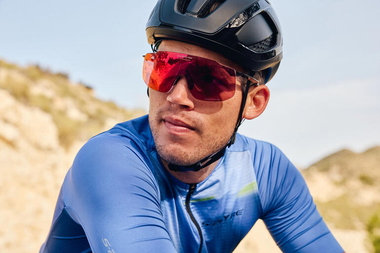 Cycliste portant des lunettes de soleil sport rouges et un casque noir sur un sentier.