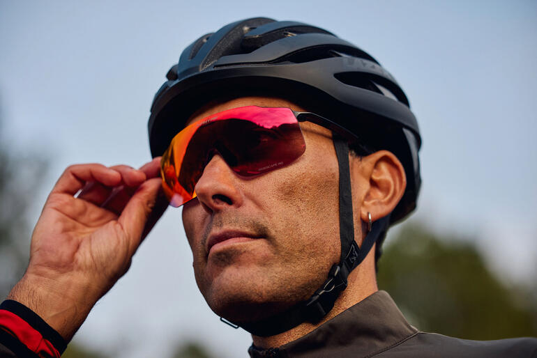 Homme portant des lunettes de soleil sport rouges et un casque noir, ajustant ses lunettes.