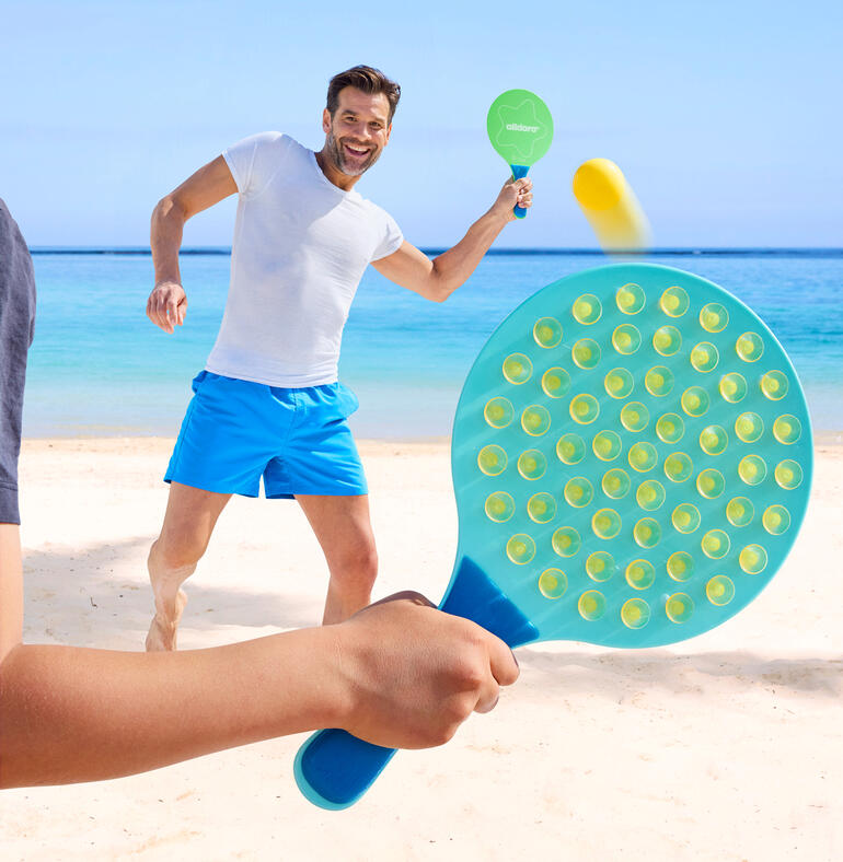 Homme jouant sur la plage avec une raquette ovale et frappant la balle.
