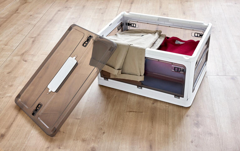 Boîte de rangement ouverte avec des vêtements sur un sol en bois.