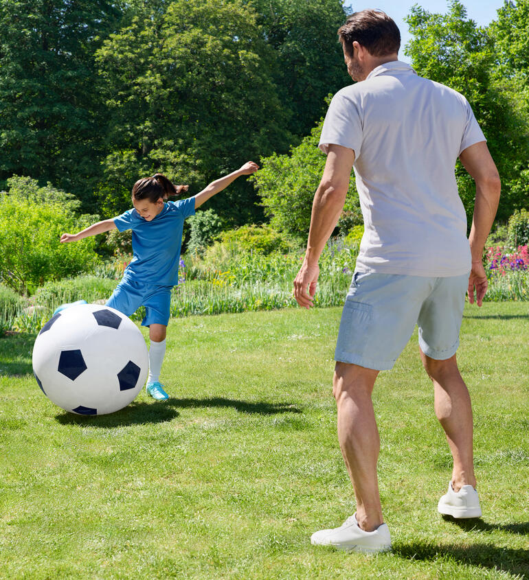 Un garçon joue avec un grand ballon de football dans le jardin.