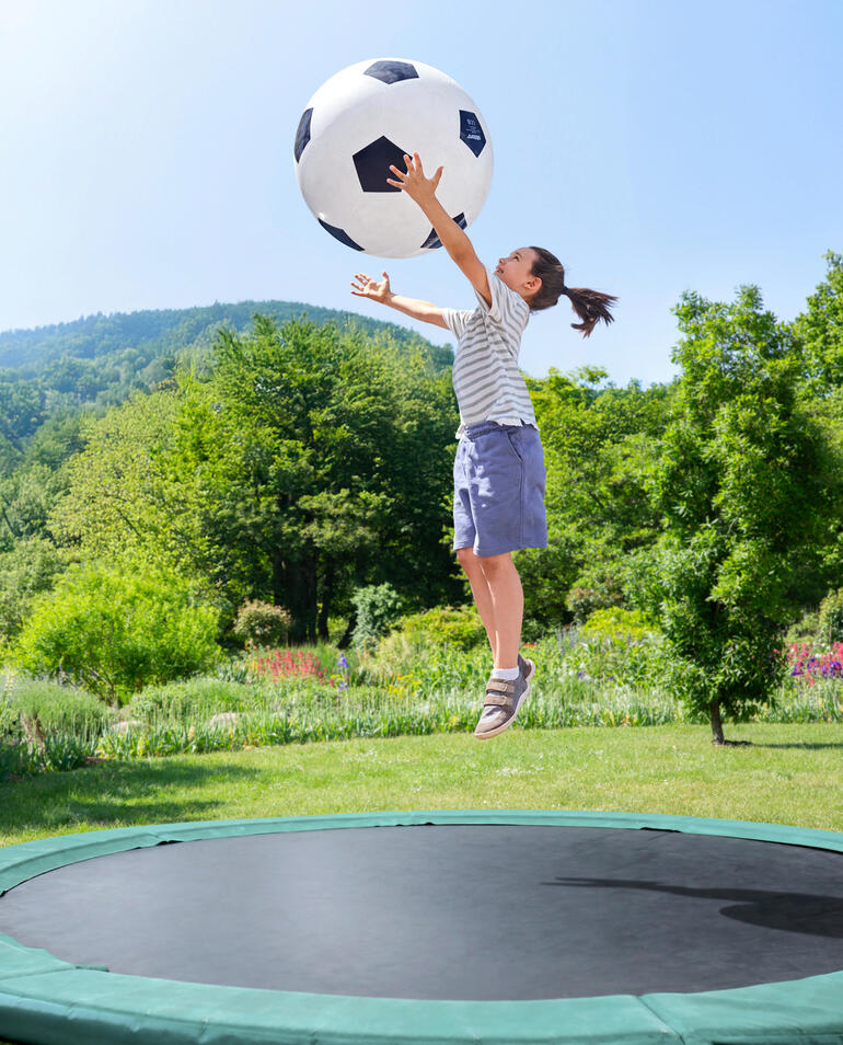 Une fille saute dans le jardin et attrape un grand ballon de foot.
