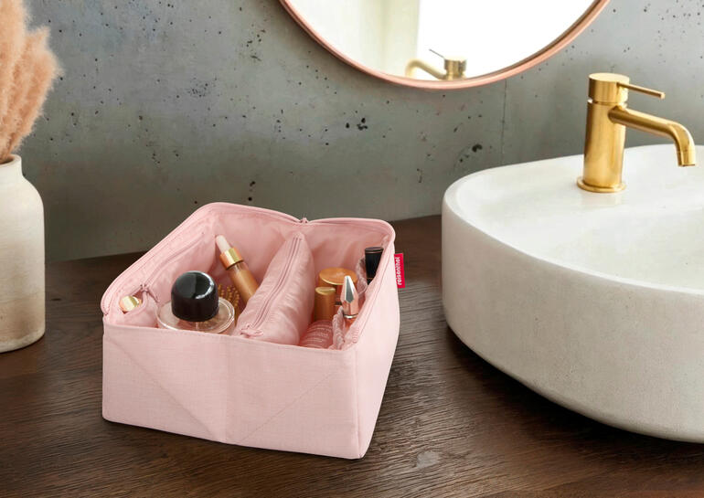 Nécessaire de voyage 2-en-1 rose ouverte avec des produits de soin sur une table en bois
