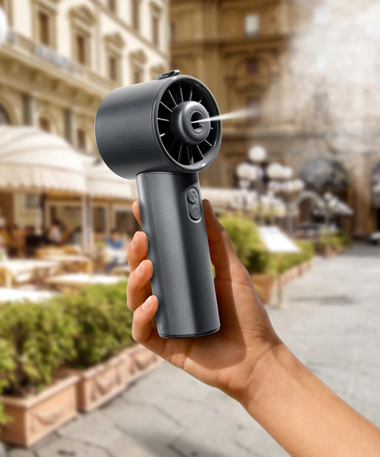 Main tenant un Hydro-Mini-ventilateur dans une ville, avec des bâtiments historiques en arrière-plan.