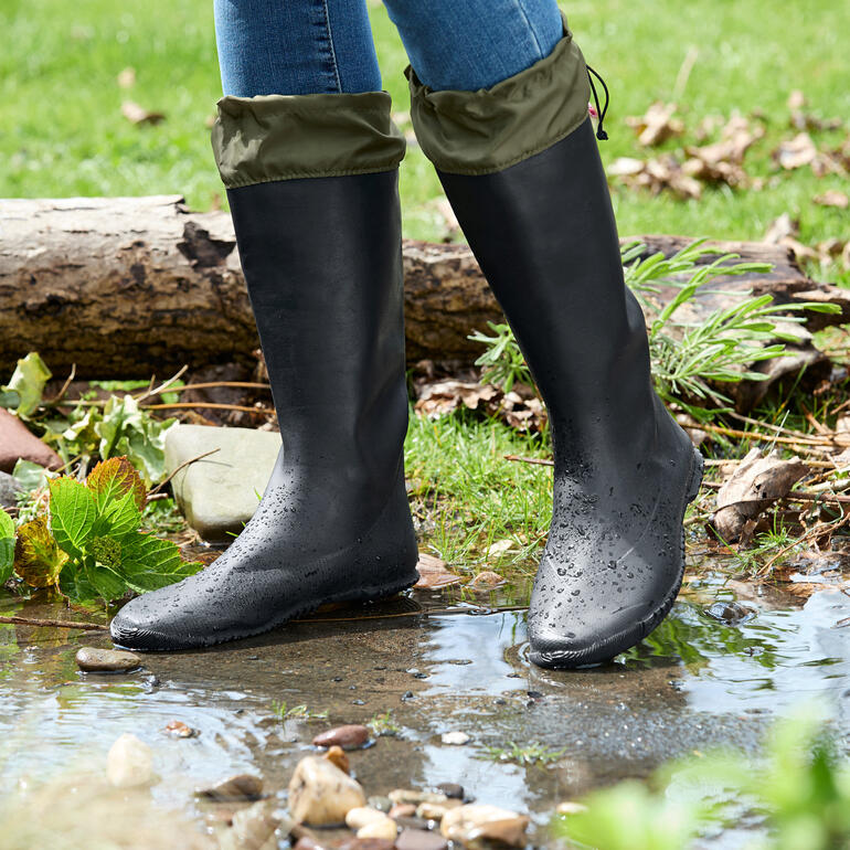 Bottes en caoutchouc noires avec le haut replié, se tenant au bord d'un ruisseau.