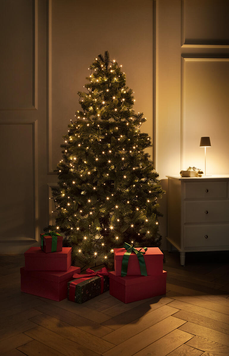 Sapin de Noël illuminé avec des cadeaux et une lumière chaleureuse dans une pièce élégante.