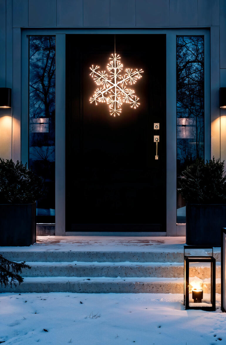 Flocon de neige LED éclairé à l'extérieur, suspendu devant une porte d'entrée.