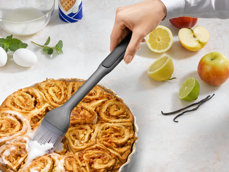 Main avec un pinceau à pâtisserie qui badigeonne un gâteau à la cannelle chaud.