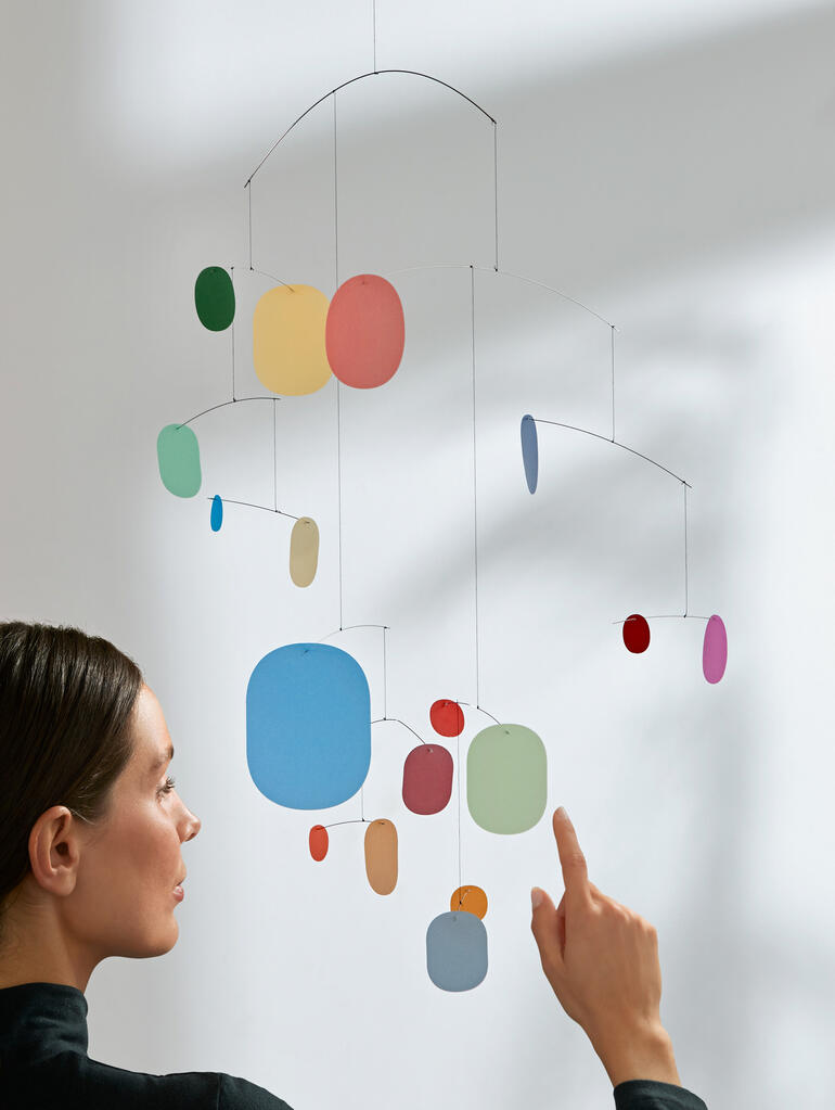 Une femme pointe du doigt un mobile coloré sur un mur.